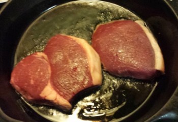 Steaks hit the pan with a little extra virgin olive. Oil is just beginning to “stand up” under heat, and not smoking at all. Steaks very lightly sizzle on contact.