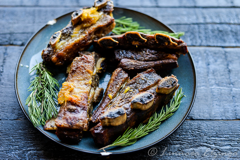 Beef short ribs with orange glaze and rosemary garnish on a blue plate. 