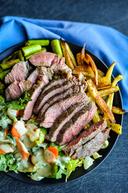 Sliced steak paired with potato fries and a side salad with homemade dressing.