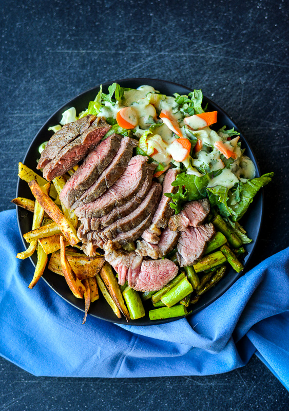 Sliced sirloin tip steak with sides on a black plate. 