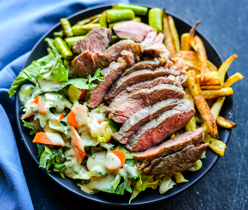 Slices of steak with potato fries and salad on the side. 