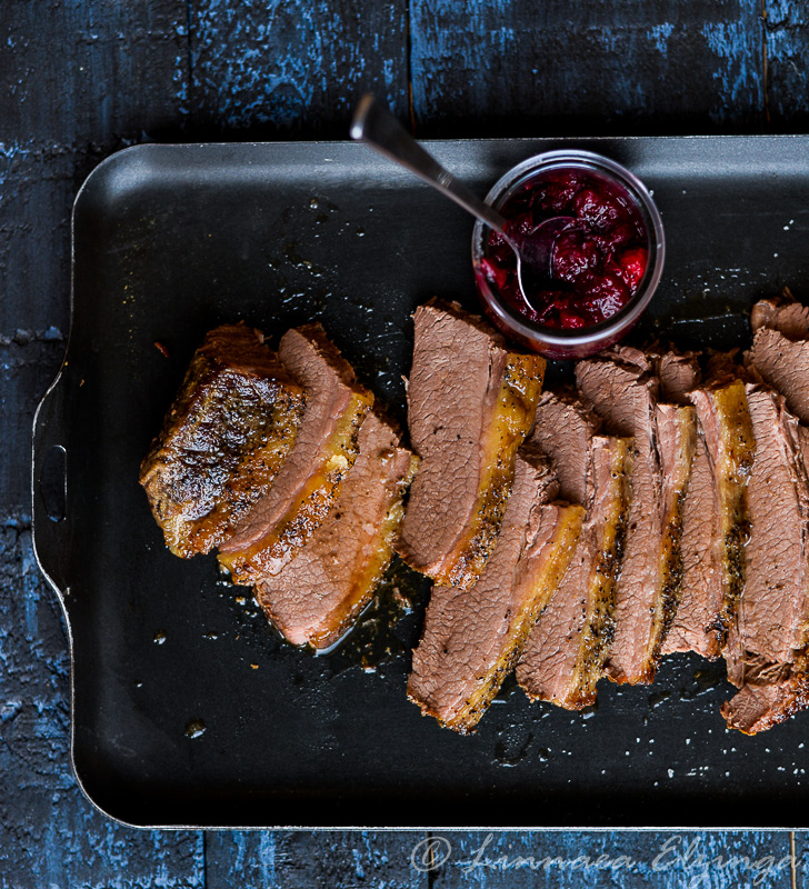 Festive sliced brisket roast with a side of cranberry sauce. 