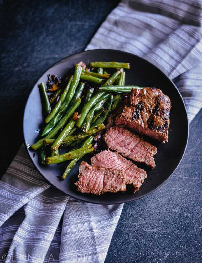 Sliced new york steak with grill marks and sauteed green beans and onions. 