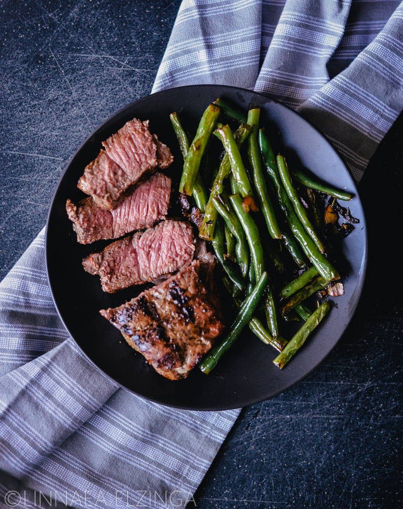 New York steak sliced and served with green beans on a black background. 